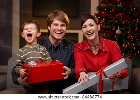 Happy parents and son sitting at couch, holding christmas gifts, laughing.?