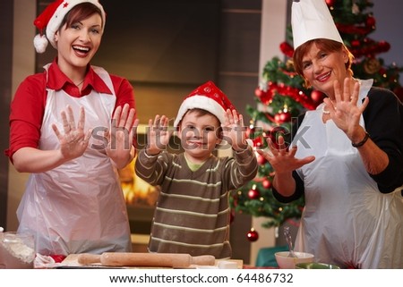 Portrait of happy child with mom and grandmother at christmas baking, raising doughy hands, smiling.?