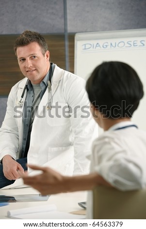 Two medical doctors chatting in doctor\'s room, smiling.