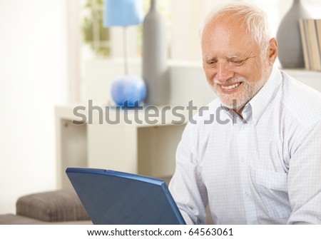 Portrait of aged man at home looking at laptop computer screen, smiling.