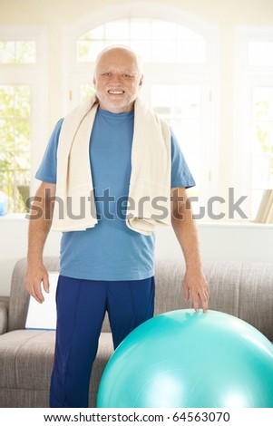 Active senior exercising with fit ball at home, smiling at camera.