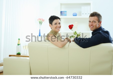 Romantic man giving red rose to woman at home, smiling.?