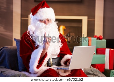 Modern Santa Claus sitting by fireplace using computer computer.?