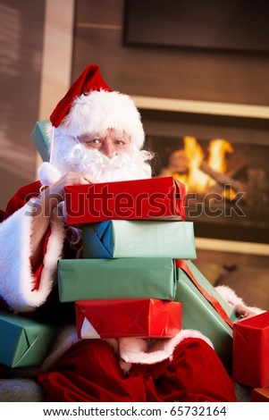 Portrait of Santa Claus sitting by fireplace holding a pile of Christmas presents.?