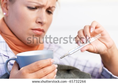 Young female at home having flu, feeling bad, taking her temperature, drinking hot tea in bed.?