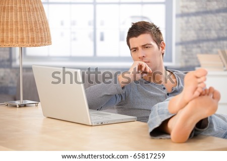 stock photo Young man sitting at home with bare feet on desk thinking