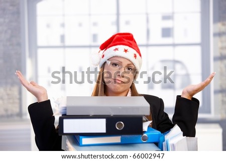 Young woman in santa hat sitting in office behind folders, having trouble.?