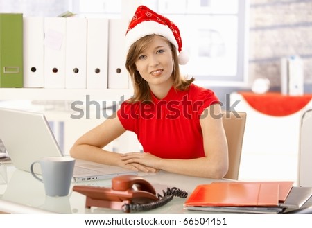 Female office worker sitting at office desk, wearing xmas hat.?