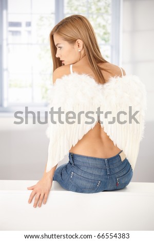 Young woman sitting front of window, wearing angel wings, back view.?