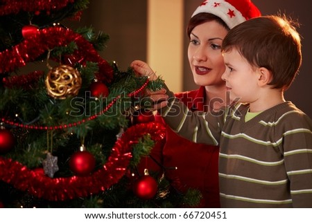 Mother helping little boy to decorate christmas tree at home.?