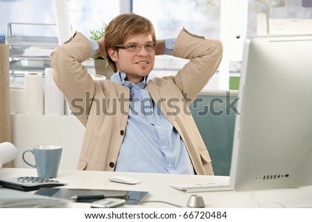 Confident businessman sitting at office desk, using computer, looking at screen, smiling.?