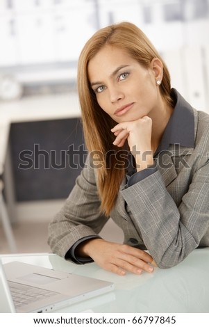 Portrait of smart businesswoman sitting at desk with laptop computer, thinking, looking at camera.?