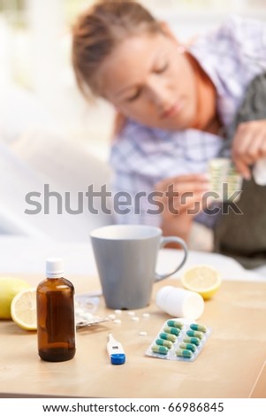 Vitamins, medicines, hot tea and lemons in front, woman caught cold taking medicines in background.?