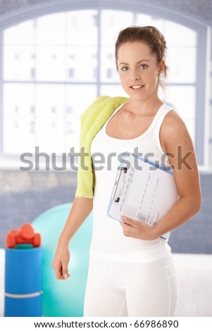 Pretty young girl prepared for personal training in gym, holding her training plan in hand.?