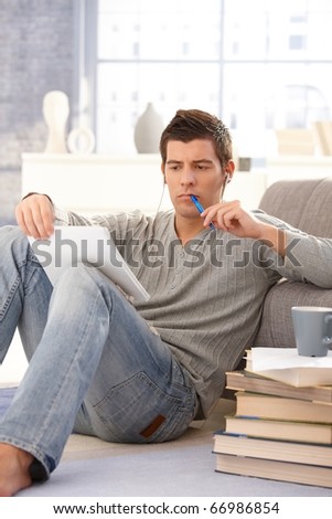 College student concentrating on studying sitting on living room floor with books and notes and pen.?