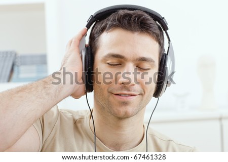 Casual man listening music with headphones at home, relaxing with closed eyes, smiling.