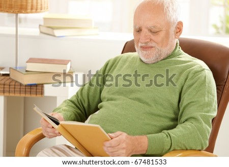 Old man sitting at home reading book in armchair.