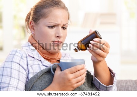 Young female at home having flu, feeling bad, taking medicine, vitamin, drinking hot tea in bed.