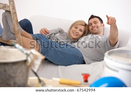 Smiling couple lying together after painting, man pointing at funny detail, woman laughing.?