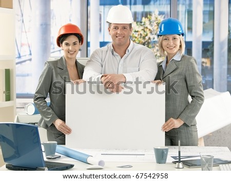 Portrait of confident architect team wearing hardhat, holding blank poster for copyspace.?