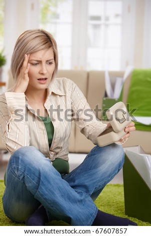 Shocked woman sitting at home looking at money box, looking troubled.?