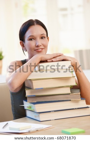 Smiling university student girl sitting at desk with pile of books.?