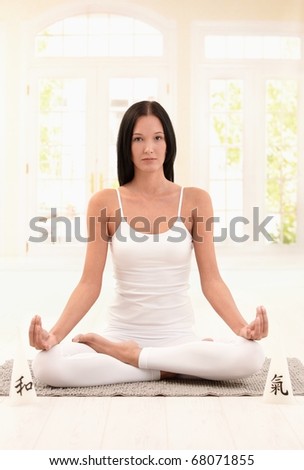 Attractive woman practicing yoga in lotus posture on ground, looking at camera.?