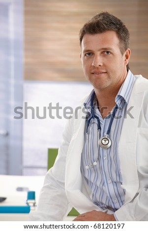 Portrait of smiling doctor in consulting room wearing white smock and stethoscope around neck.