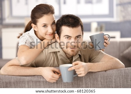Happy couple sitting on sofa at home, drinking tea, smiling.