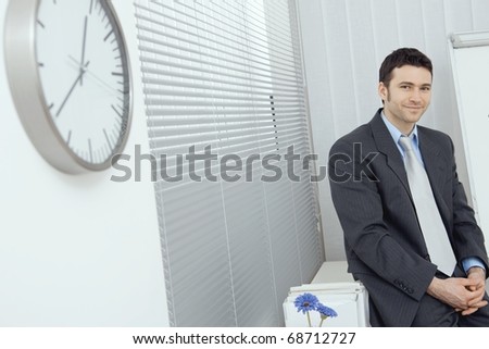 Portrait of businessman wearing grey suit and blue shirt, sitting in office, smiling.?