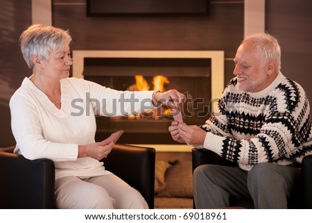 Senior couple playing cards on winter night in front of fireplace.?