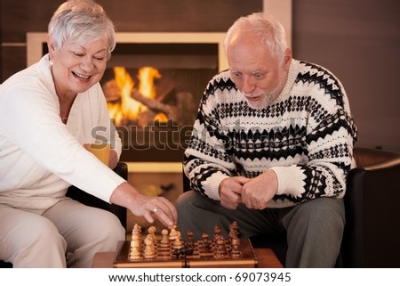Senior couple having fun with chess at home on winter night woman moving chess man on board, man looking surprised.