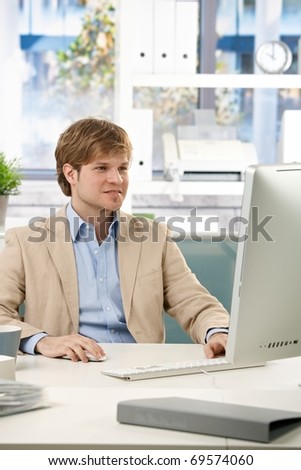 Happy businessman sitting at desk in office working with computer, looking at screen.?
