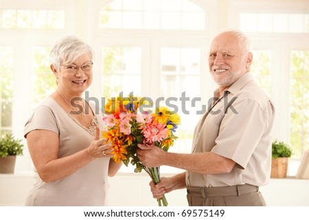 Portrait of happy senior couple with colorful bouquet of flowers, smiling at camera.?