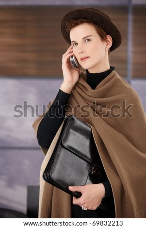 Trendy professional with briefcase on mobile phone call, leaving office.?