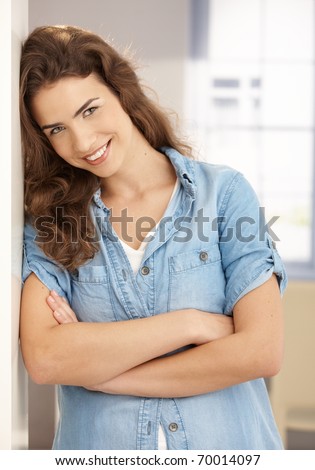 Happy young female smiling arms crossed at home, leaning against wall.  .?