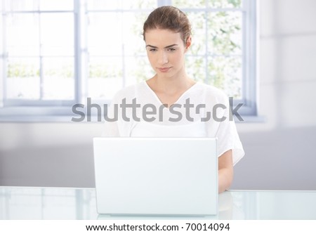 Young attractive female using laptop at home front of window.?