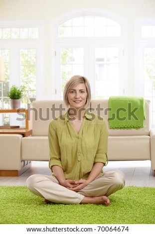 Happy  woman sitting with legs crossed on living room floor, looking at camera.?