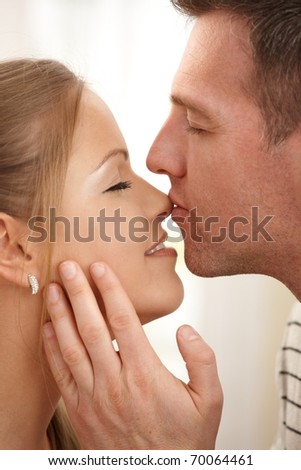 Man kissing happy woman\'s nose and stroking neck with eyes closed in closeup.?