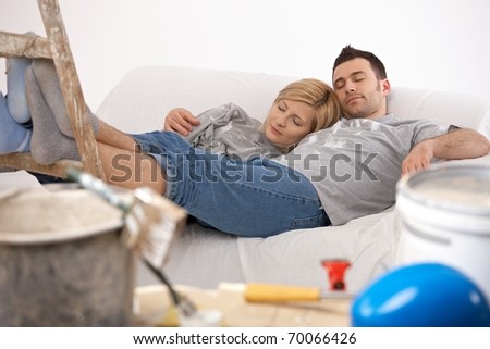 Couple lying together after painting with closed eyes, relaxing after hard work with feet up on ladder.?