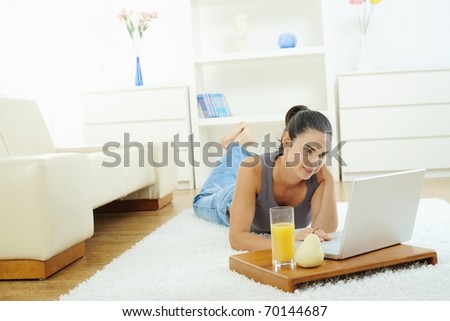 Young woman lying on floor at home and working on laptop computer, looking at screen.?