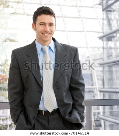 Portrait of happy young businessman standing on office corridor looking at camera, smiling.?