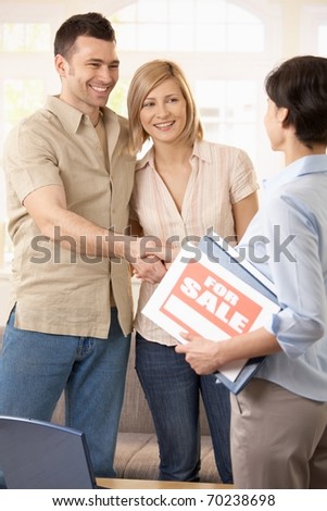 Happy couple making deal with estate agent, shaking hands.?