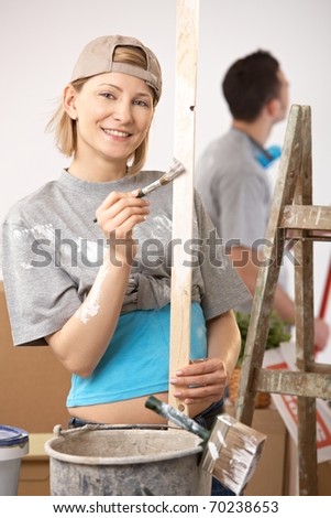 Portrait of smiling woman painting, working on new house, boyfriend standing in background.?