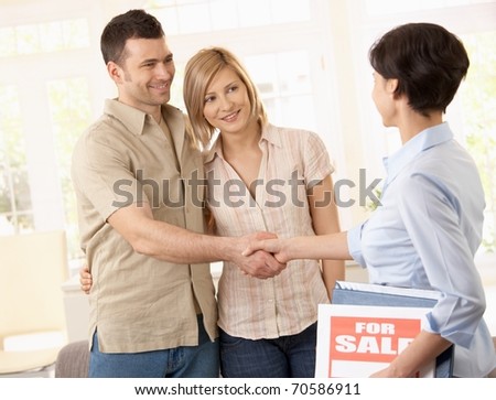 Estate agent congratulating young couple on making deal on new house.?