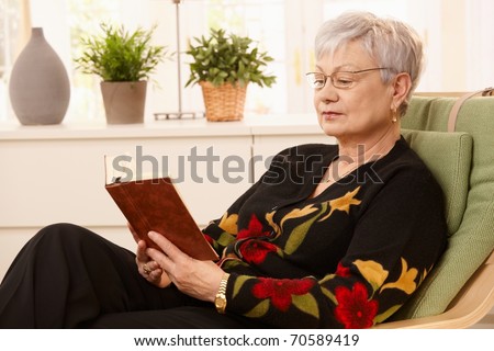 Portrait of pensioner reading in armchair in bright living room.?