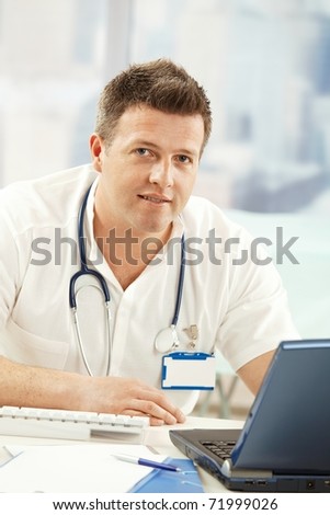 Portrait of confident doctor smiling at camera sitting at desk with computer.?