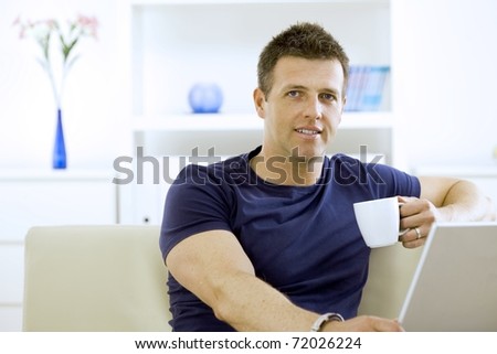 Relaxed young man drinking coffee at home, sitting on couch.?