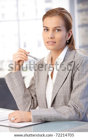 Pretty businesswoman sitting at desk in bright office, writing notes.?