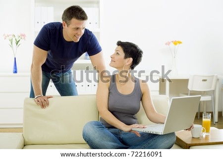 Happy young couple browsing internet on laptop computer at home, smiling.?